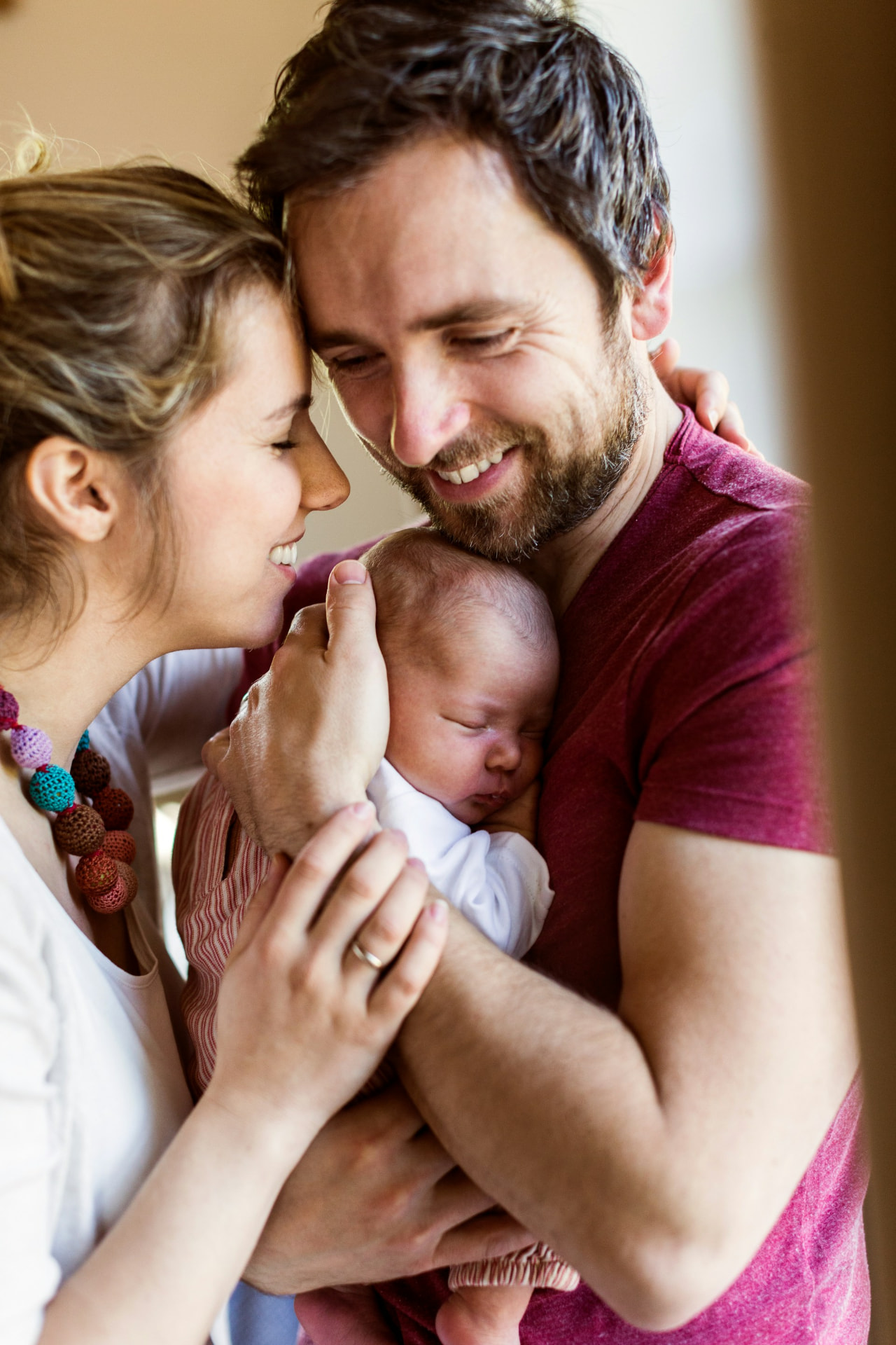 Smiling parents holding their sleeping newborn close together