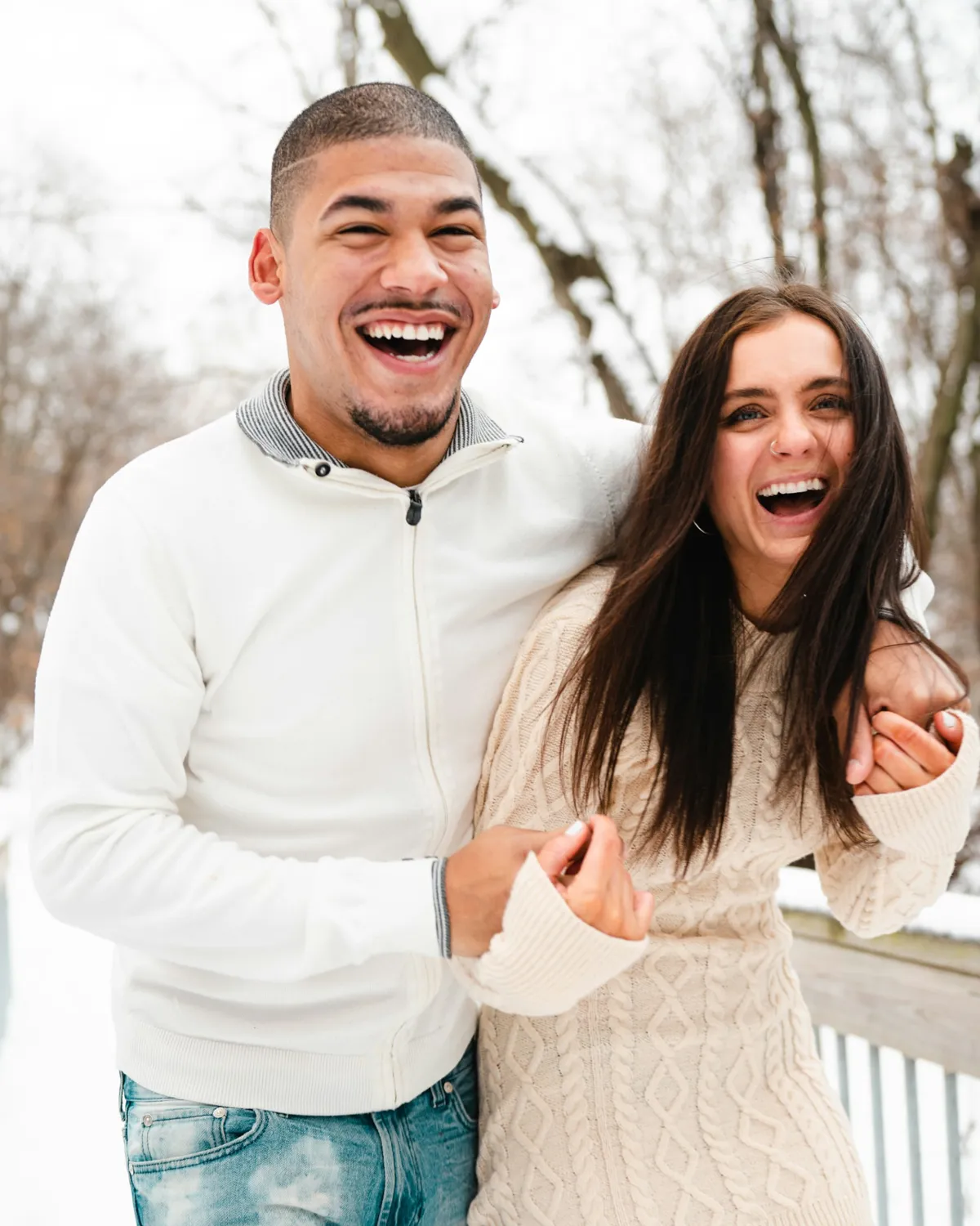 A young couple laughing arm in arm outdoors in the snow