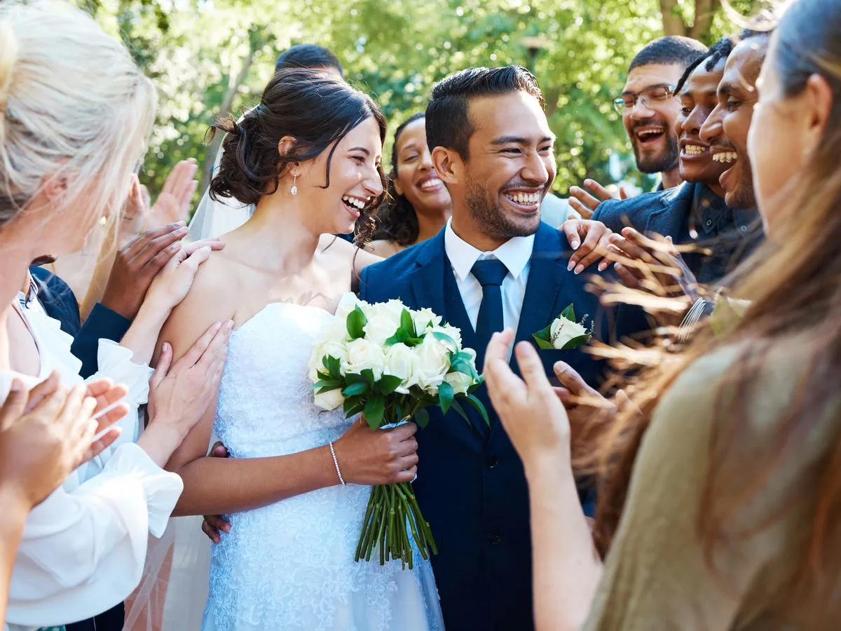 A bride and groom surrounded by smiling wedding guests outdoors