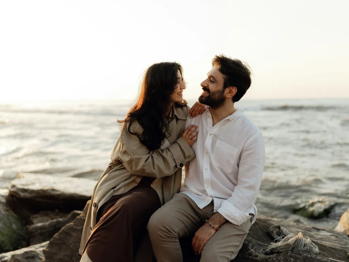 A smiling couple sitting together on the rocks by the sea